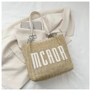 Detailed view of straw tote bag with white leather straps and metallic chain handle