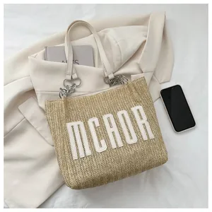 Close-up of woven straw tote bag featuring leather MCAOR lettering and metal chain handles