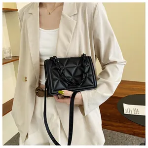 Detail of black quilted crossbody bag with chunky acrylic chain on a beige blazer