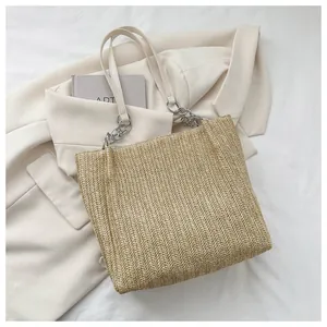 Detail view of woven straw tote bag featuring beige leather strap and silver chain accent