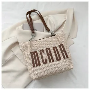 Detail of straw tote bag with leather letters MCAOR and metal ring strap connectors
