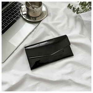 Detail of a black patent leather envelope wallet with glossy finish on white fabric