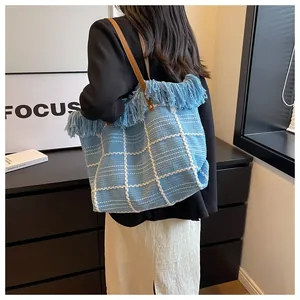 Detail of blue checkered woven tote bag with fringe edge and brown leather handles