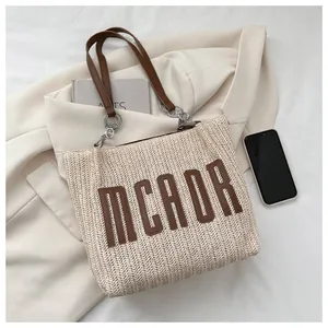 Detail of straw tote bag showing MCAOR leather lettering and metal chain handle attachment