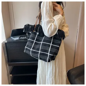 Detail of checkered woven tote bag with black fringe trim and brown slim shoulder straps