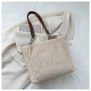 Close-up of woven straw tote bag featuring brown leather straps and silver chain details