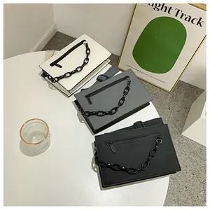 Three minimalist envelope bags in white, grey, and black with chunky chain decoration