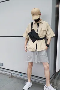 Détail d'un sac bandoulière en nylon noir porté avec une chemise utilitaire kaki