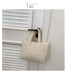 Détail d'un sac cabas matelassé blanc crème avec coutures verticales suspendu à une porte