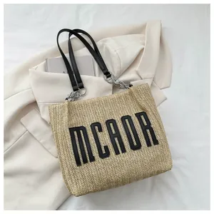 Detail of woven straw tote with MCAOR lettering and black leather chain shoulder strap