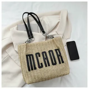Detail of straw tote bag with black MCAOR letter patch and leather chain strap