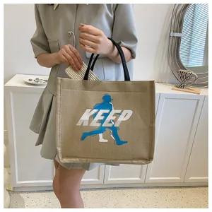 Detail of khaki canvas tote bag with black woven handles and blue Keep print graphic