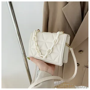 Detail of white quilted crossbody bag with decorative thick acrylic chain and gold hardware