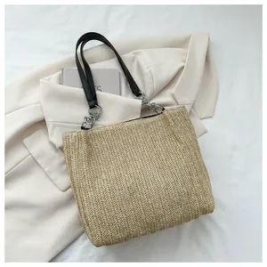 Detail of beige straw tote bag featuring herringbone weave and black leather chain straps