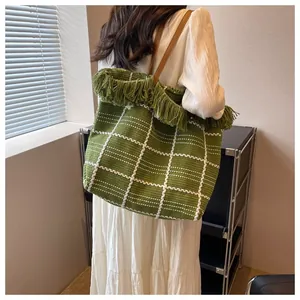 Detail of green woven tote bag with white grid pattern, tassels and brown leather strap