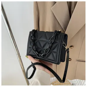 Detail of black quilted shoulder bag featuring thick acrylic chain and gold metal hardware