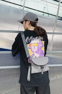 Détail du sac bandoulière en nylon gris avec boucle de fermeture et poche zippée latérale