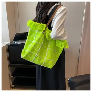 Close-up of fluorescent green knit tote bag featuring white grid patterns and fringe detail