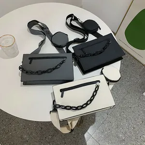 Three minimalist crossbody square bags in grey, black, and beige with chain detail