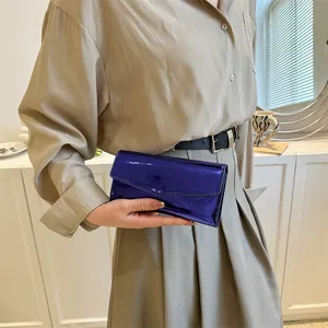 Minimalist envelope wallet in metallic royal blue glossy patent leather held by a model