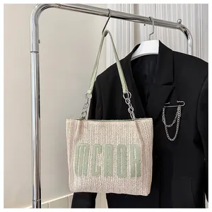 Detail of woven straw tote bag featuring green MCAOR patch and metal chain strap