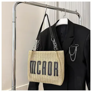 Detail of woven straw bucket bag featuring MCAOR embroidery and chain leather strap