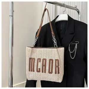 Detail of woven straw tote bag featuring brown MCAOR lettering and leather chain strap