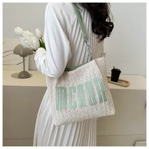 Detail of woven straw tote bag with green leather MCADR letter patch and chain strap