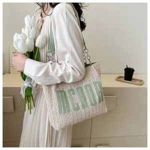 Detail of hand-woven straw tote bag with green leather accents and letter embroidery