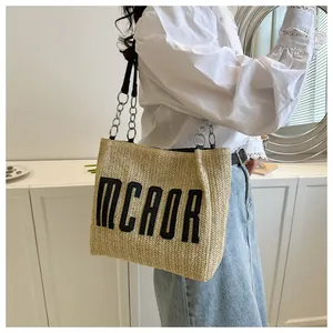 Detailed view of large straw tote bag featuring black MCAOR embroidery and chain straps