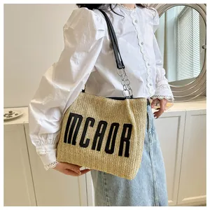 Detail of straw woven tote bag with MCAOR embroidery and metal chain strap on a model