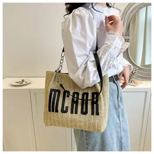 Detail of straw tote bag featuring MCAOR letter patch and silver metal chain strap