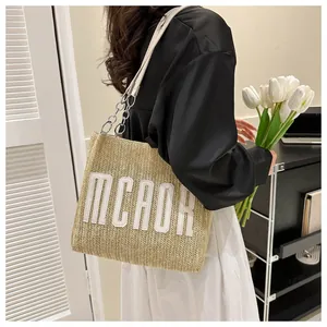 Detail of straw tote bag with white MCAOR letters and metal chain strap on model