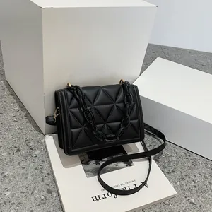 Quilted black crossbody bag with bold acrylic chain and gold metal hardware on geometric props