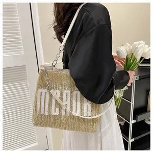 Detail of a straw tote bag with white leather trim and silver metal chain strap