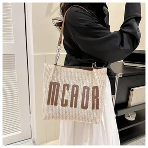 Close-up of straw tote bag with MCAOR logo patch and leather chain shoulder strap