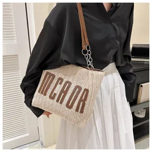 Detail of woven straw tote bag featuring brown MCAOR letters and metal chain strap