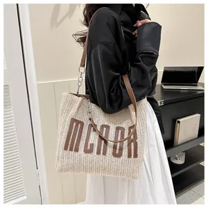 Detailed view of straw tote bag with brown leather MCADR letter patch and chain strap