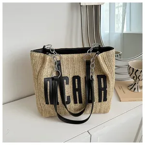 Detail of straw tote bag showing beige woven texture with black DCAOR lettering