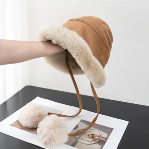 Detail of camel plush bucket hat featuring soft faux suede and fluffy white pom-pom ties