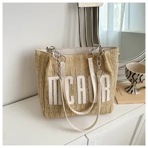Detail view of woven straw tote bag with white leather letter patches and chain strap