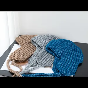 Women's knit trapper hats in brown, grey, and blue colors with earflaps and long ties