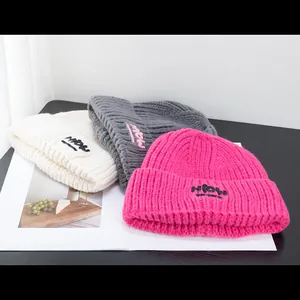 Drei Strickmützen in Beige, Dunkelgrau und Rosa mit HiOW-Logo-Stickerei auf dem Umschlag