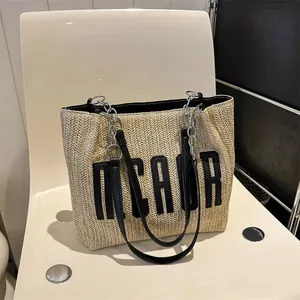 Large beige woven straw tote bag with black NCAUR embroidery and chain shoulder straps