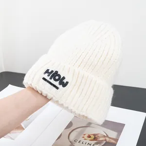 Nahaufnahme einer weißen Strickmütze mit schwarzem HiOW-Patch und Wollstruktur-Finish