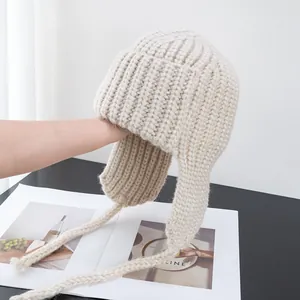 Detailed close-up of beige chunky ribbed knit trapper hat with braided earflaps ties