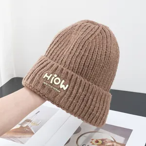 Detailansicht einer dunkelbraunen Strickmütze mit Rippenmuster und gelbem Buchstabenaufnäher