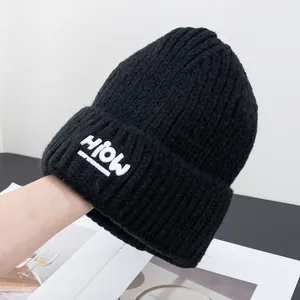 Nahaufnahme einer schwarzen Strickmütze mit weißem HiOW-Aufnäher und umgeschlagenem Rand