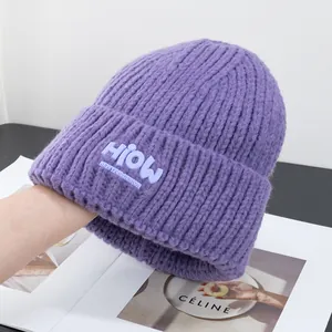 Nahaufnahme der lila Strickmütze mit HIOW Design-Label und gerippter Strickstruktur