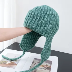 Detailed view of sage green thick-knit trapper hat with long earflaps for winter warmth
